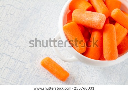 Baby carrot sticks in white bowl on light blue wood background, top view