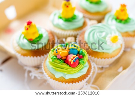 Easter cupcakes with eggs, chicks and flower decorations in egg holder, plaid napkin, white wood background