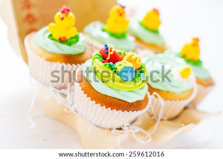 Easter cupcakes with eggs, chicks and flower decorations in egg holder, plaid napkin, white wood background