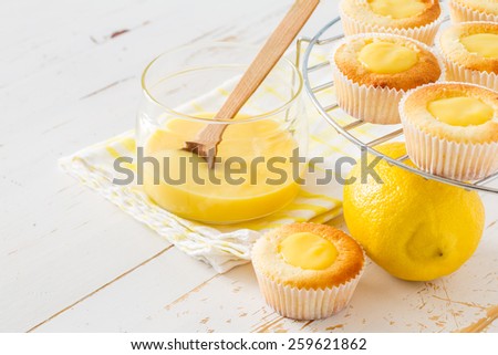 Lemon cupcakes preparation - cupcakes on wire rack, curd, lemon on white wood background