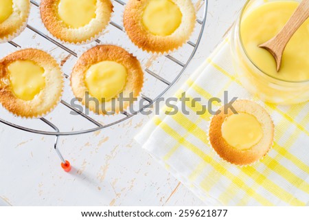 Lemon cupcakes preparation - cupcakes on wire rack, curd, on white wood background, top view