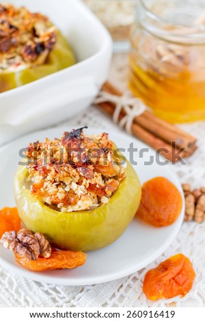 Stuffed apples with oat, raisins, walnuts, dried apricots, cinnamon and honey on white plate, white wood background, closeup