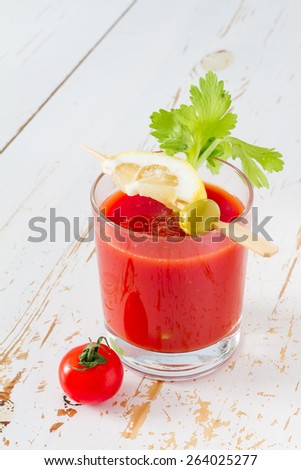 Tomato juice in glass with lemon and olive on stick and celery, cherry tomato, white wood background, closeup