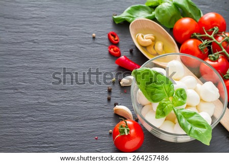 Caprese salad ingredients - cherry tomatoes, mozzarella, basil leafs, olive oil, nuts, chili, garlic, on dark stone background, top view