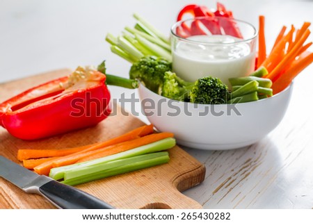 White bowl with carrot, celery, pepper, broccoli and green beans, yogurt sauce, white wood background