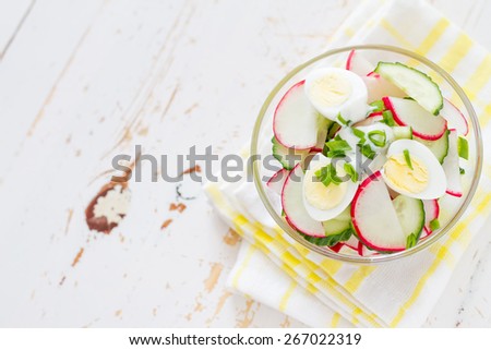 Radish, cucumber, egg, dill, onion yogurt salad in glass bowl, plaid napkin, white wood background, top view