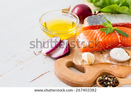 Salmon fillet with spinach, salt, pepper, garlic, oil, white wood background, closeup