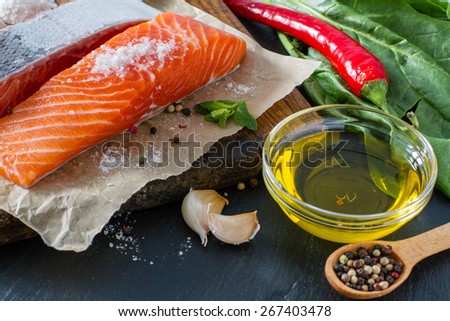 Salmon fillet with spinach salt, pepper, garlic, oil, dark stone background, closeup