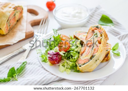 Strudel pie with salmon and spinach, served on white plate with salad, cherry tomatoes, sour cream, white wood background, closeup