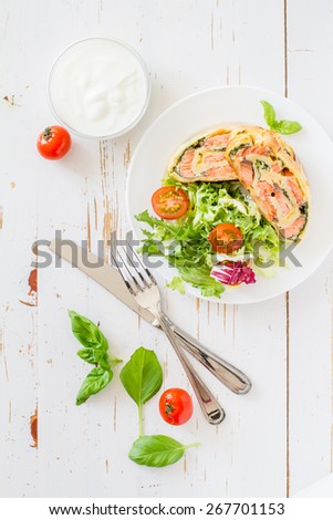 Strudel pie with salmon and spinach, served on white plate with salad, cherry tomatoes, sour cream, white wood background, top view