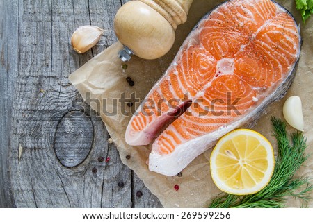 Salmon steak with lemon slices, garlic, herbs in baking paper, rustic wood background, top view