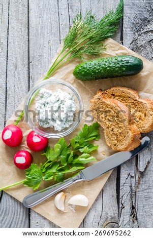 Bruschetta with cottage cheese and radish, herbs, cucumber, garlic, knife, rustic wood background, top view