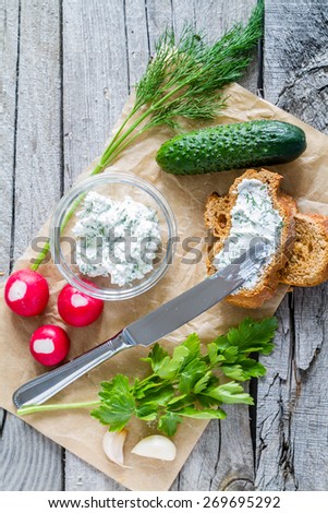 Bruschetta with cottage cheese and radish, herbs, cucumber, garlic, knife, rustic wood background, top view