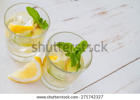 Ginger lemonade and ingredients - ginger, lemon, lime, mint, sugar, ice, white wood background