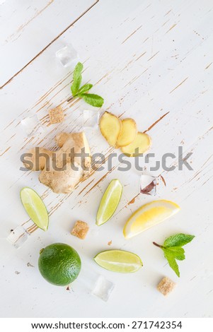 Ginger lemonade ingredients - ginger, lemon, lime, mint, sugar, ice, white wood background, top view