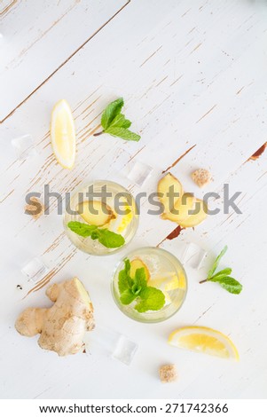 Ginger lemonade and ingredients - ginger, lemon, lime, mint, sugar, ice, white wood background, top view