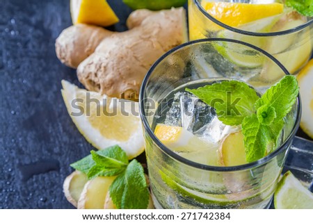 Ginger lemonade and ingredients - ginger, lemon, lime, mint, sugar, ice, dark stone background, water drops, closeup