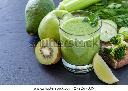 Green smoothie and ingredients - avocado, apple, celery, cucumber, broccoli, kiwi, dill, parsley, lime, dark stone background