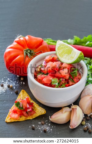 Salsa sauce and ingredients - tomato, chili, onion, garlic, parsley, lime, pepper, nacho, dark stone background