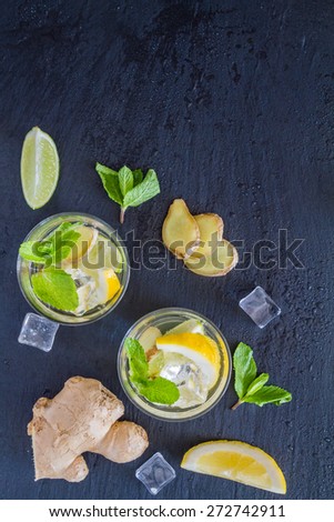 Ginger lemonade and ingredients - ginger, lemon, lime, mint, sugar, ice, dark stone background, top view