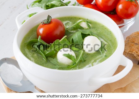 summer ruccola pure soup with cherry tomato and bread, baking paper, white wood background, closeup