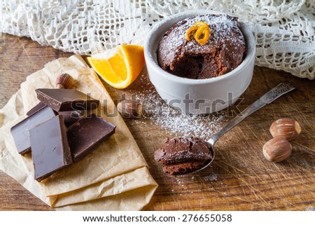 Chocolate orange muffin in white bowl, orange slice, nuts, chocolate, wood board, knitted napkin
