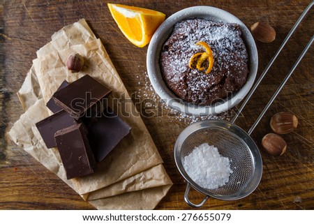 Chocolate orange muffin in white bowl, orange slice, nuts, chocolate, wood board, top view
