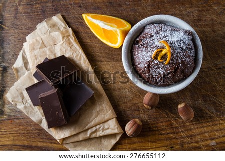 Chocolate orange muffin in white bowl, orange slice, nuts, chocolate, wood board, top view