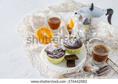 Chocolate and orange cupcakes, nuts, orange slice, chocolate, coffee maker, white plates, knitted napkins, white wood background