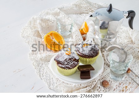 Chocolate and orange cupcakes, nuts, orange slice, chocolate, coffee maker, white plates, knitted napkins, white wood background