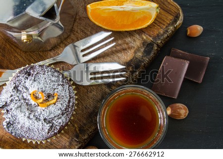 Chocolate and orange cupcakes, nuts, orange slice, chocolate, coffee maker, wood board, dark stone background, top view