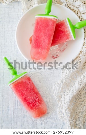 Watermelon fruit ice pops on white plate, knitted napkin, rustic light blue background, top view