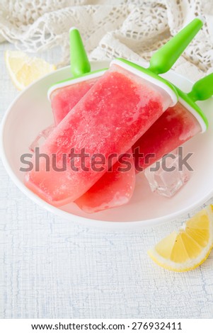 Watermelon fruit ice pops on white plate, knitted napkin, rustic light blue background