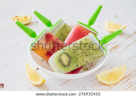 Watermelon, kiwi, berry fruit ice pops on white plate, white wood background