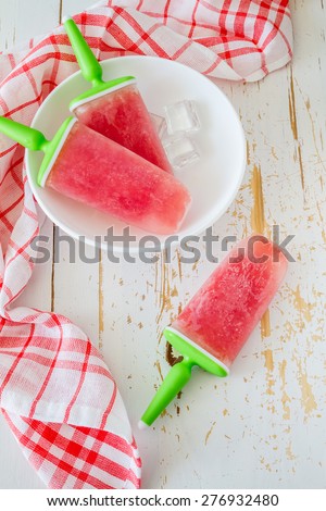 Watermelon fruit ice pops on white plate, plaid napkin, white wood background, top view