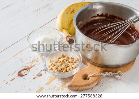 Banana pops preparation - banana, chocolate, nuts, coconut powder, white wood background