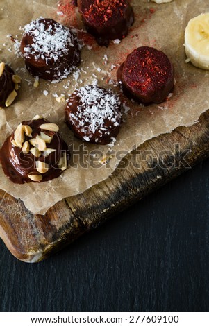 Banana pops preparation - banana, nuts, coconut powder, chocolate, baking paper, wood board, top view