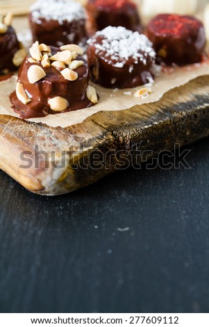 Banana pops preparation - banana, nuts, coconut powder, chocolate, baking paper, wood board, closeup