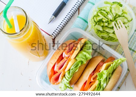 Lunch box - sandwiches, salad, juice, notepad, pen, white wood background