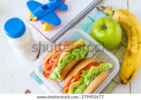 Lunch box for school - sandwiches, milk, toy, notepad, apple, banana, white wood background, top view
