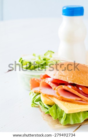 Lunch box - sandwich, milk, salad, white wood background