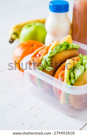 Lunch box - sandwiches, milk, apple, orange, banana, juice, white wood background