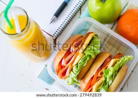 Lunch box - sandwiches, apple, orange, juice, notepad, pen, white wood background