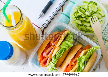 Lunch at a workplace - sandwiches, milk, juice, salad, notepad, pen, white wood background, top view