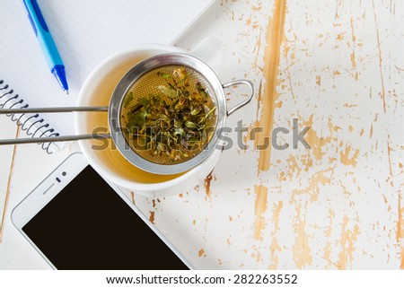 Breakfast - notepad, phone, tea, flowers, white wood background, top view