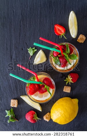 Strawberry lemonade and ingredients - strawberry, lemon, sugar, ice, dark stone background, top view