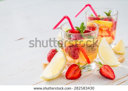Strawberry lemonade in glass and ingredients - strawberry, lemon, sugar, ice, white wood background