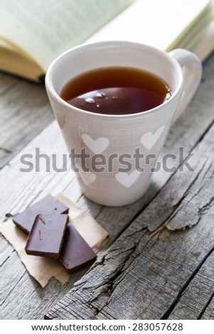 Morning snack - book, tea, chocolate on rustic wood background, closeup