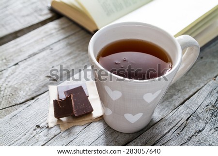 Morning snack - book, tea, chocolate on rustic wood background