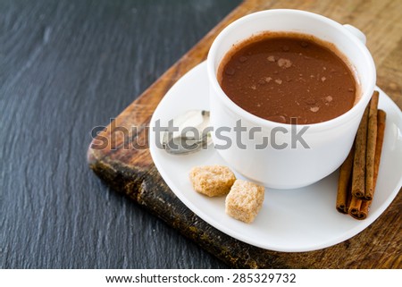 Hot chocolate, cinnamon sticks, sugar in white cup, dark stone background